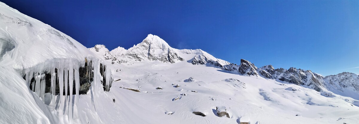 Panoramaaufnahme im Winter. Zentral zu sehen ist der Großglockner. Im Vordergrund links hängen ein paar Eiszapfen von einem Felsvorsprung. 